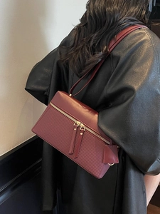 Chic burgundy leather handbag with woven texture detail, modeled on a black coat