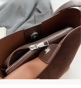 Detail of silver smooth zipper and magnetic closure on brown matte leather tote bag