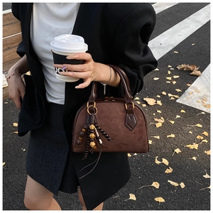 Close-up of retro dark brown pillow bag with beaded tassel detail against autumn street