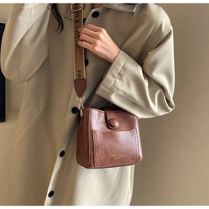 Détail d'un sac seau en cuir marron avec large bandoulière imprimée et texture grainée