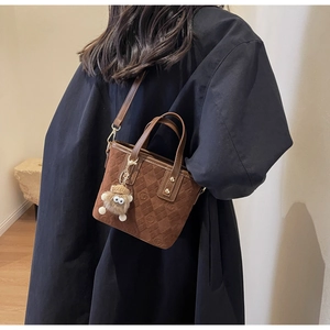 Close-up of brown suede bucket bag featuring embossed monogram texture and furry monster charm