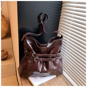 Dettaglio di borsa hobo in pelle lucida marrone scuro con doppie fibbie su legno