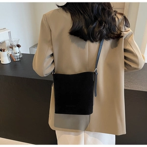 Detailed view of the matte black bucket bag worn with a beige blazer in a modern cafe