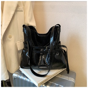Dettaglio borsa tote in pelle nera lucida con cinturino a fibbia in un set minimalista
