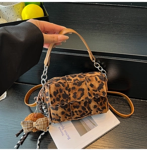 Detail of leopard print crossbody bag with woven panels, silver chain and plush charm