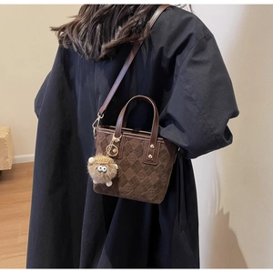 Detail of dark brown suede tote with embossed logo patterns and a cute plush lamb charm