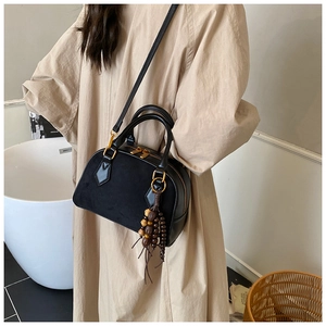 Detail of black suede patchwork pillow bag with gold zippers and decorative wood bead tassel