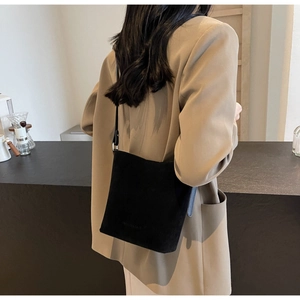 Side view of matte black suede bucket bag worn by model in a minimalist cafe setting