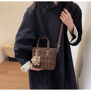 Detail of vintage brown bucket bag with embossed logo and a white sheep keychain accessory