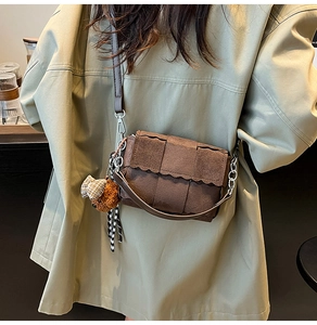 Close-up of brown woven shoulder bag with a teddy bear charm and checkered ribbon detail