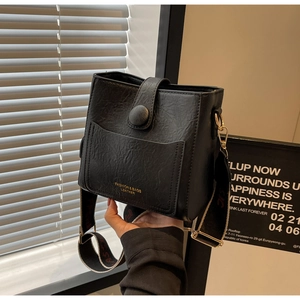 Détail du sac seau noir texturé avec logo doré et large bandoulière en tissu robuste