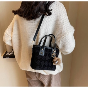 Close-up of black quilted bucket bag with matte finish and plush pendant on model