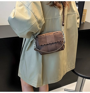 Detail view of brown suede woven crossbody bag with wavy flap and silver chain strap
