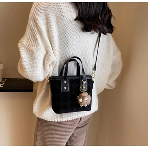 Detail of black quilted bucket bag with gold strap and plush charm on white sweater