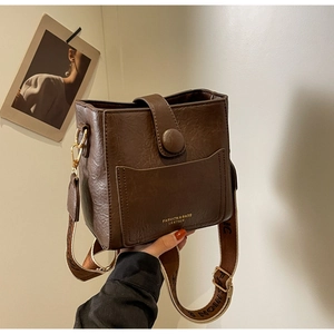 Détail du sac seau en cuir marron foncé avec texture grainée et bandoulière jacquard