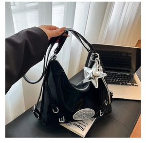 Detail of black glossy shoulder bag with silver star charm and metal hardware accents