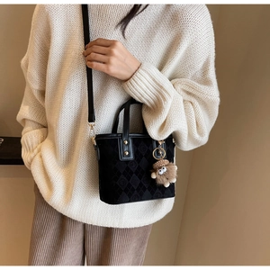 Detail of black quilted bucket bag with golden hardware and fuzzy monster keychain charm