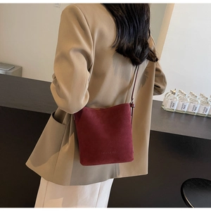 Detail of burgundy frosted leather bucket bag with shoulder strap shown on a model