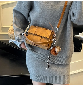 Chic brown woven crossbody bag featuring a wave-cut flap and cute teddy bear charm