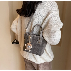 Detail of grey suede bucket bag with letter embossing and cute monster charm