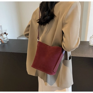 Burgundy matte suede crossbody bucket bag with embossed logo detail on model