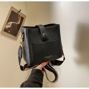 Détail d'un sac seau en cuir noir texturé avec bandoulière tissée et finitions dorées