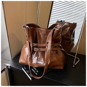 Dettaglio di una borsa a secchiello in pelle marrone con fibbie e barra logo in metallo