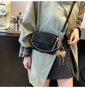 Detail of woven black crossbody bag with matte texture and cute teddy bear charm
