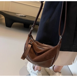 Detail of a dark brown suede saddle bag with adjustable strap worn by a female model