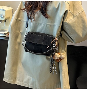 Detail of black crossbody bag with scalloped edges and cute brown bear charm pendant