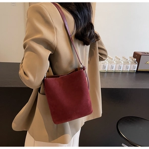 Detail of burgundy suede bucket bag with FASHION & BAGS embossed logo and slim strap