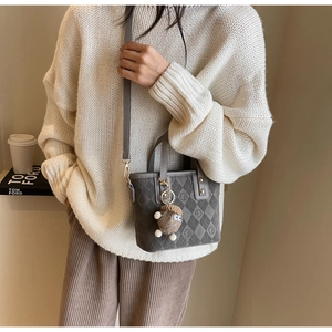 Detail of grey quilted tote bag with CF logo and plush bear charm in autumn setting