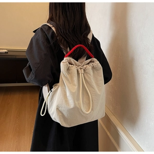 Dettaglio borsa beige con vistoso manico in corda intrecciata rossa indossata dal modello
