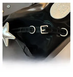 Detail of glossy black patent leather backpack with silver star charm and metal brand plate