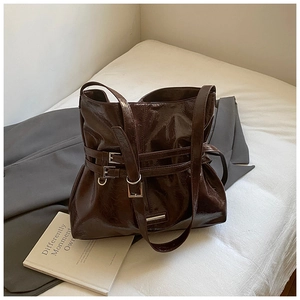 Detail of deep brown glossy tote bag with dual buckle strap on white bedding