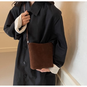 Detail of dark brown suede bucket bag with leather strap worn on a black wool coat