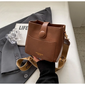 Détail du sac seau en cuir marron avec fermoir rond et large bandoulière tissée élégante