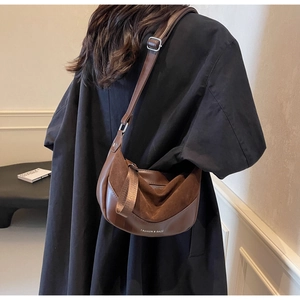 Detail of a brown half-moon saddle bag with wide shoulder strap and brand lettering