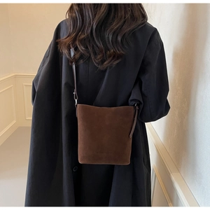 Detail of dark brown suede bucket bag with adjustable strap worn on black winter coat