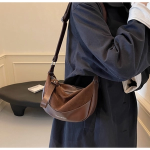 Close-up of matte dark brown crescent saddle bag featuring embossed fashion text and wide strap