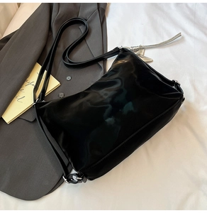Detail of glossy black patent leather shoulder bag with adjustable strap and silver hardware