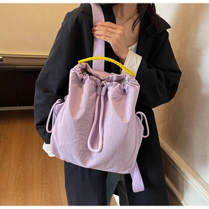 Dettaglio della borsa lilla con coulisse e manico intrecciato giallo su modella