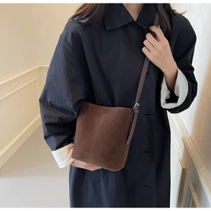 Close-up of brown matte bucket bag with adjustable strap worn on black trench coat
