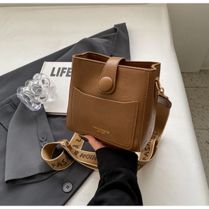 Détail du sac seau en cuir marron avec bandoulière jacquard et lettrage doré