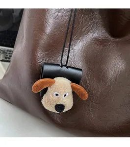 Detail of plush dog keychain on brown textured tote bag with laptop in background