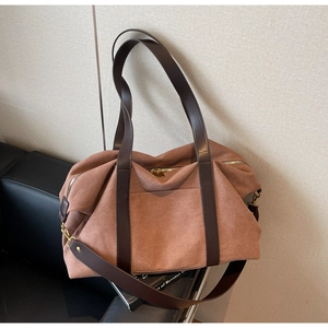 Detail of a large brown canvas tote bag with adjustable leather straps and gold metal zipper