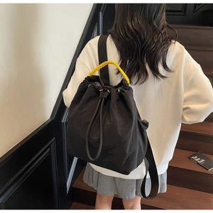 Detail of black nylon drawstring backpack featuring a contrasting yellow woven handle strap