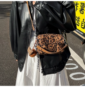 Close-up of leopard print woven crossbody bag with chain strap and bow charm detail