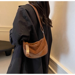 Brown leather crescent bag with wide strap shown on a model in a casual indoor setting