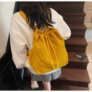 Detail of bright yellow drawstring backpack on stairs showing large capacity and nylon texture